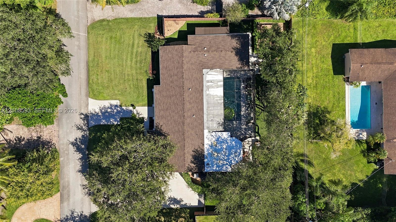 Aerial perspective featuring a multi-pitched shingle roof, paved driveway, expansive lawn, and mature trees