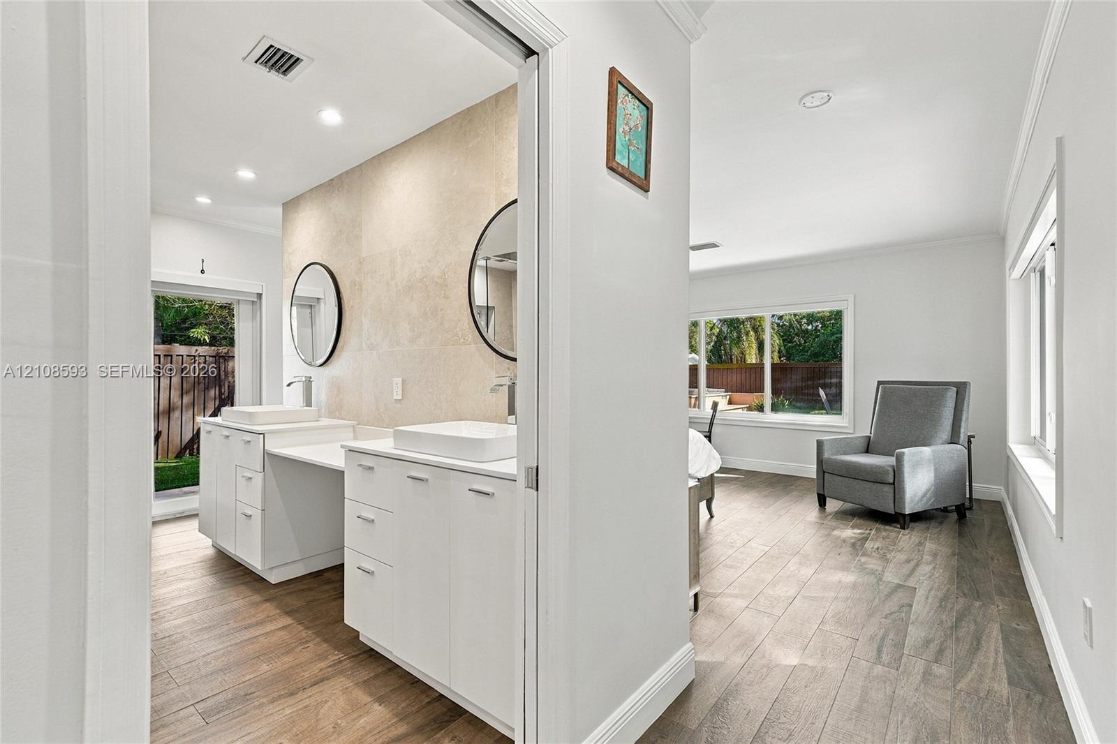 Double vanity featuring white cabinetry, square vessel sinks, and stone-tiled backsplash with circular wall-mounted mirrors and wood-finish flooring