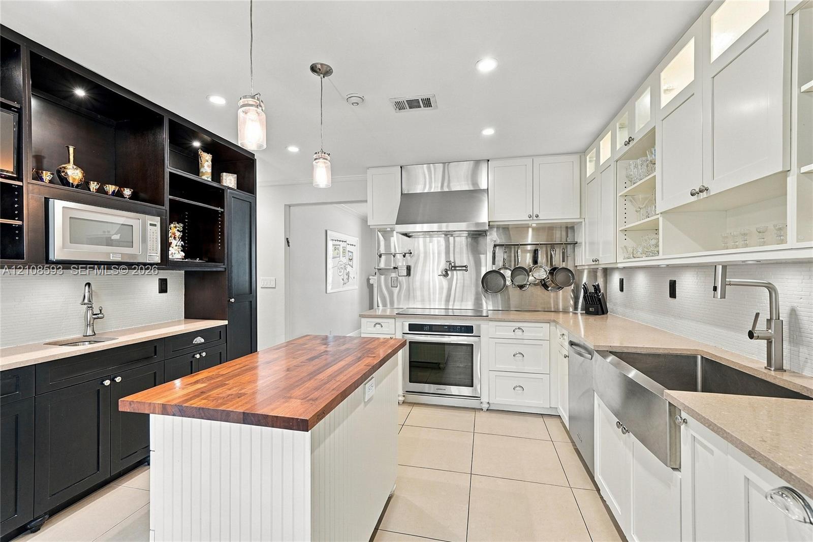 Kitchen featuring high-contrast cabinetry, butcher block island countertop, professional-grade stainless steel range hood, apron-front sink, and tiled flooring