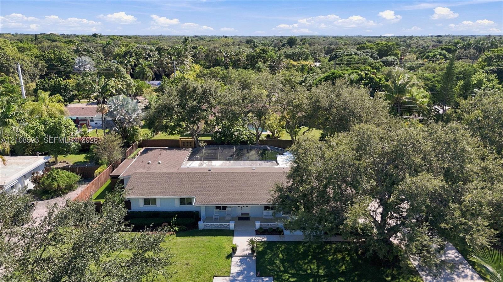 Aerial perspective featuring a single-story residence with a multi-hipped roof, a screened-in rear enclosure, a paved driveway, and mature landscaping on an expansive lot