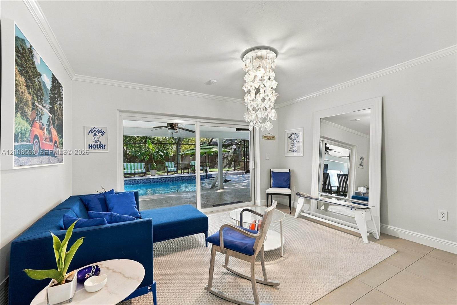 Interior space featuring crown molding, large-format tile flooring, a tiered crystal chandelier, and sliding glass doors revealing a screened-in pool Interior space featuring crown molding, large-format tile flooring, a tiered crystal chandelier, and sliding glass doors revealing a screened-in pool
