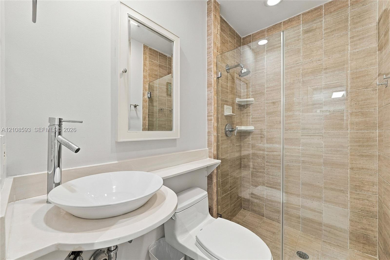 Bathroom featuring a white oval vessel sink, chrome high-arc faucet, solid surface countertop, walk-in shower with floor-to-ceiling tile, and frameless glass door