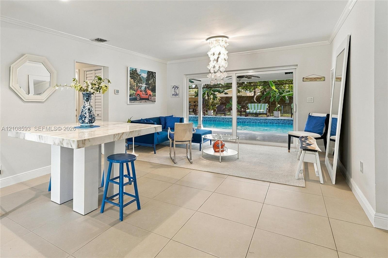 Large-format tile flooring, decorative multi-tiered light fixture, and sliding glass doors opening to an exterior swimming pool Large-format tile flooring, decorative multi-tiered light fixture, and sliding glass doors opening to an exterior swimming pool