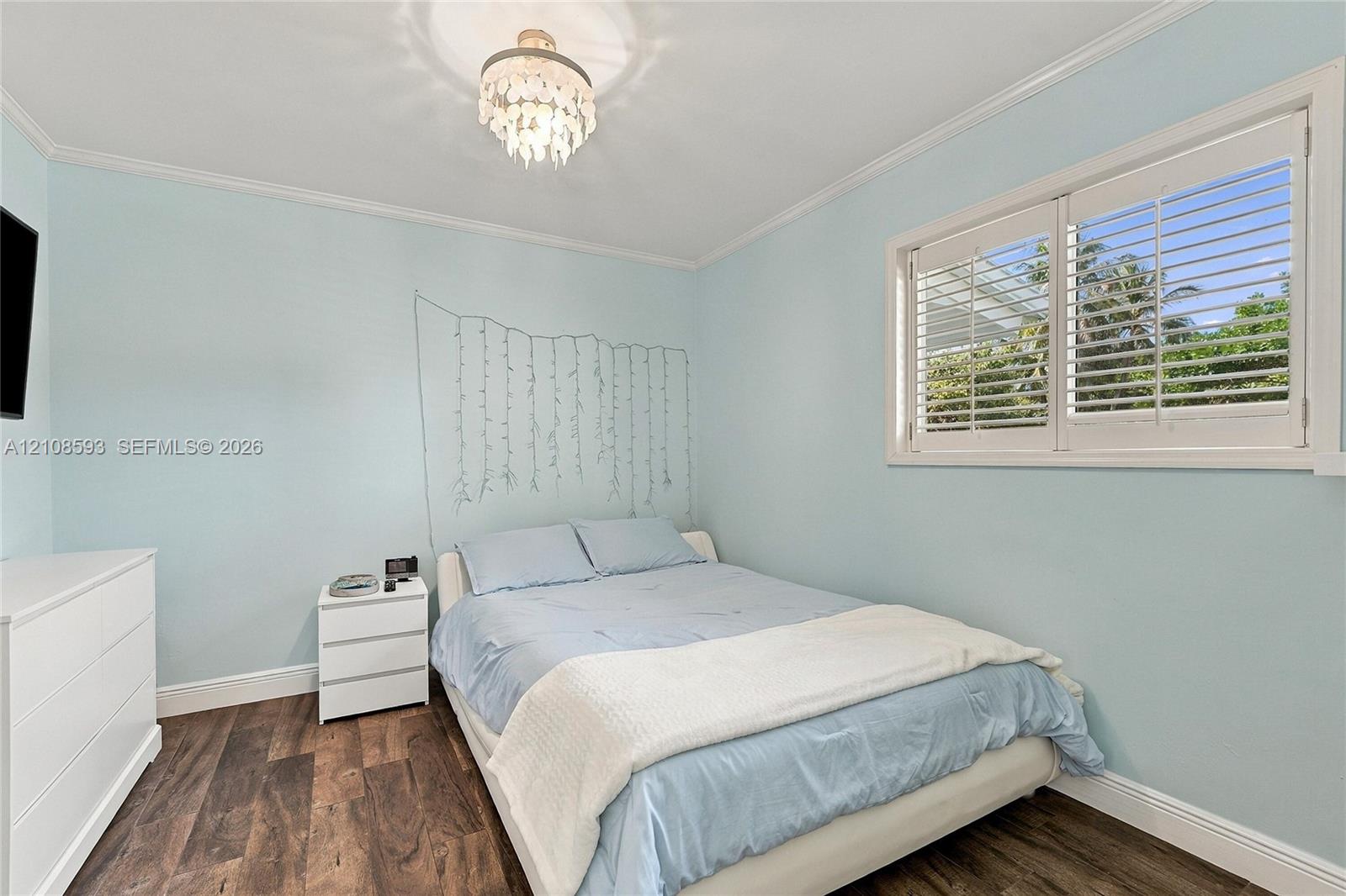 Room featuring wood-finish flooring, plantation shutters, and a decorative chandelier