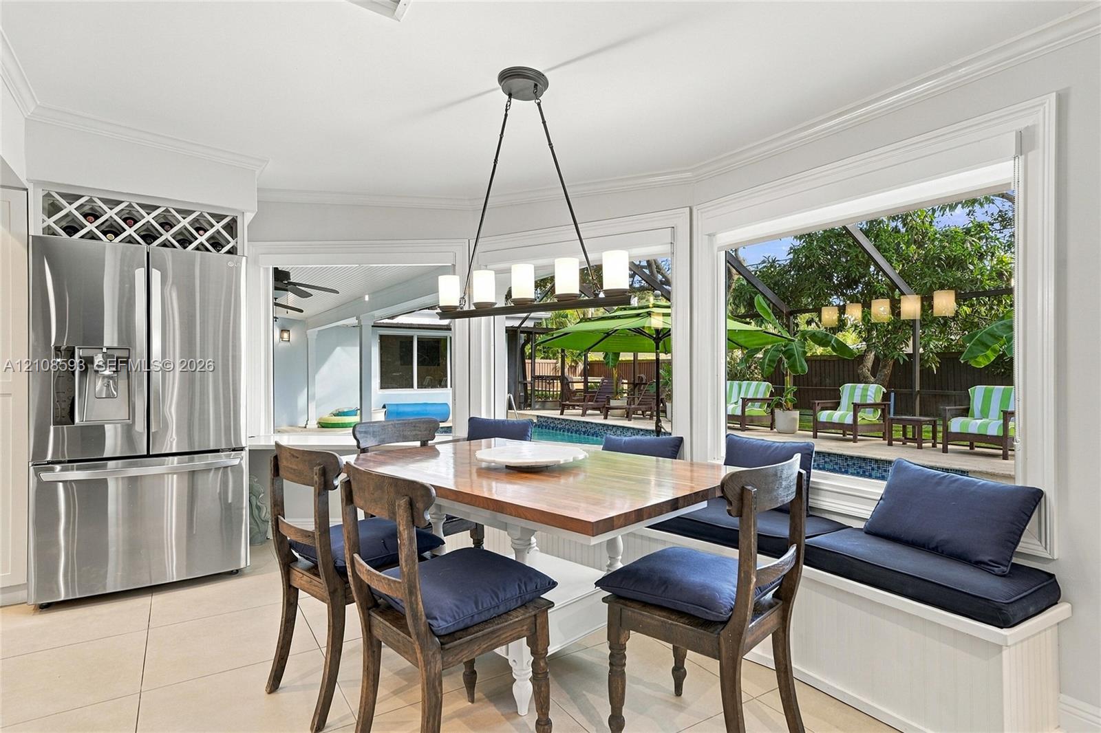 Dining area featuring large-format tile flooring, built-in window seating with integrated storage, stainless steel refrigerator with overhead wine rack, and a linear pendant light fixture
