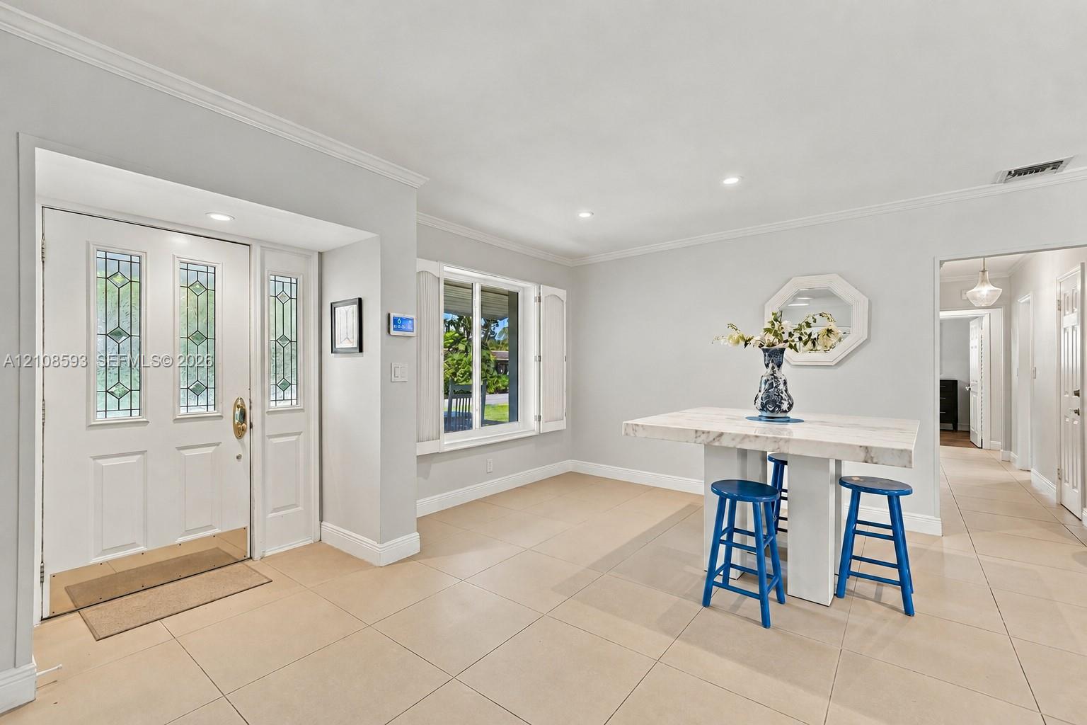 Entryway featuring a white door with decorative glass panels, neutral tile flooring, recessed lighting, crown molding, and window shutters Entryway featuring a white door with decorative glass panels, neutral tile flooring, recessed lighting, crown molding, and window shutters