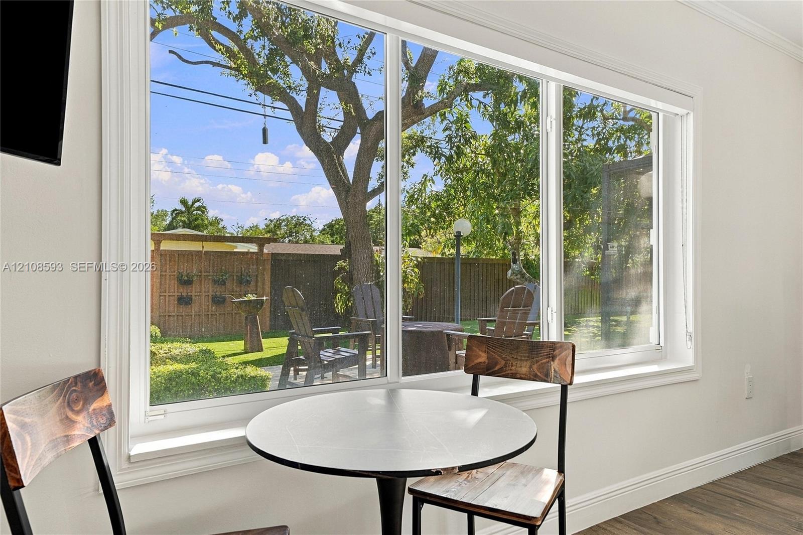 Large-scale picture window with white trim, wood-finish flooring, and backyard access featuring a wood privacy fence and mature landscaping