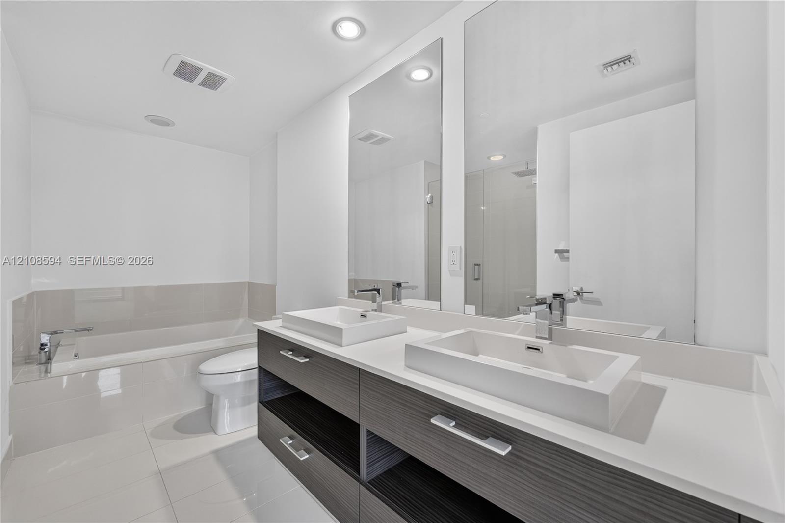 Modern floating vanity featuring dual rectangular vessel sinks, a solid surface countertop, wood-finish cabinetry, and polished chrome fixtures, complemented by floor-to-ceiling mirrors and a deep soaking tub