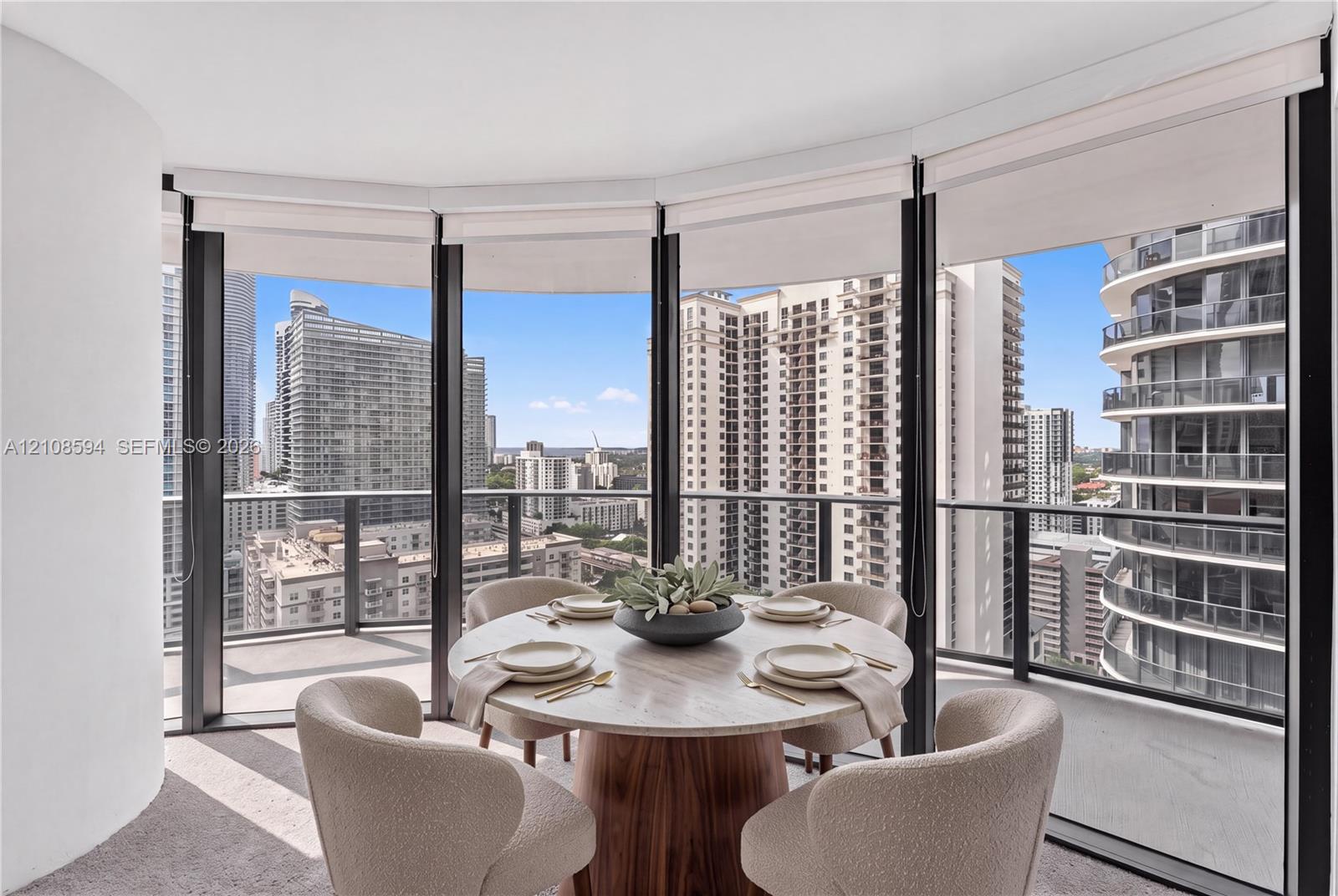 Curved floor-to-ceiling windows, wrap-around private balcony with metal railing, and neutral wall-to-wall carpeting