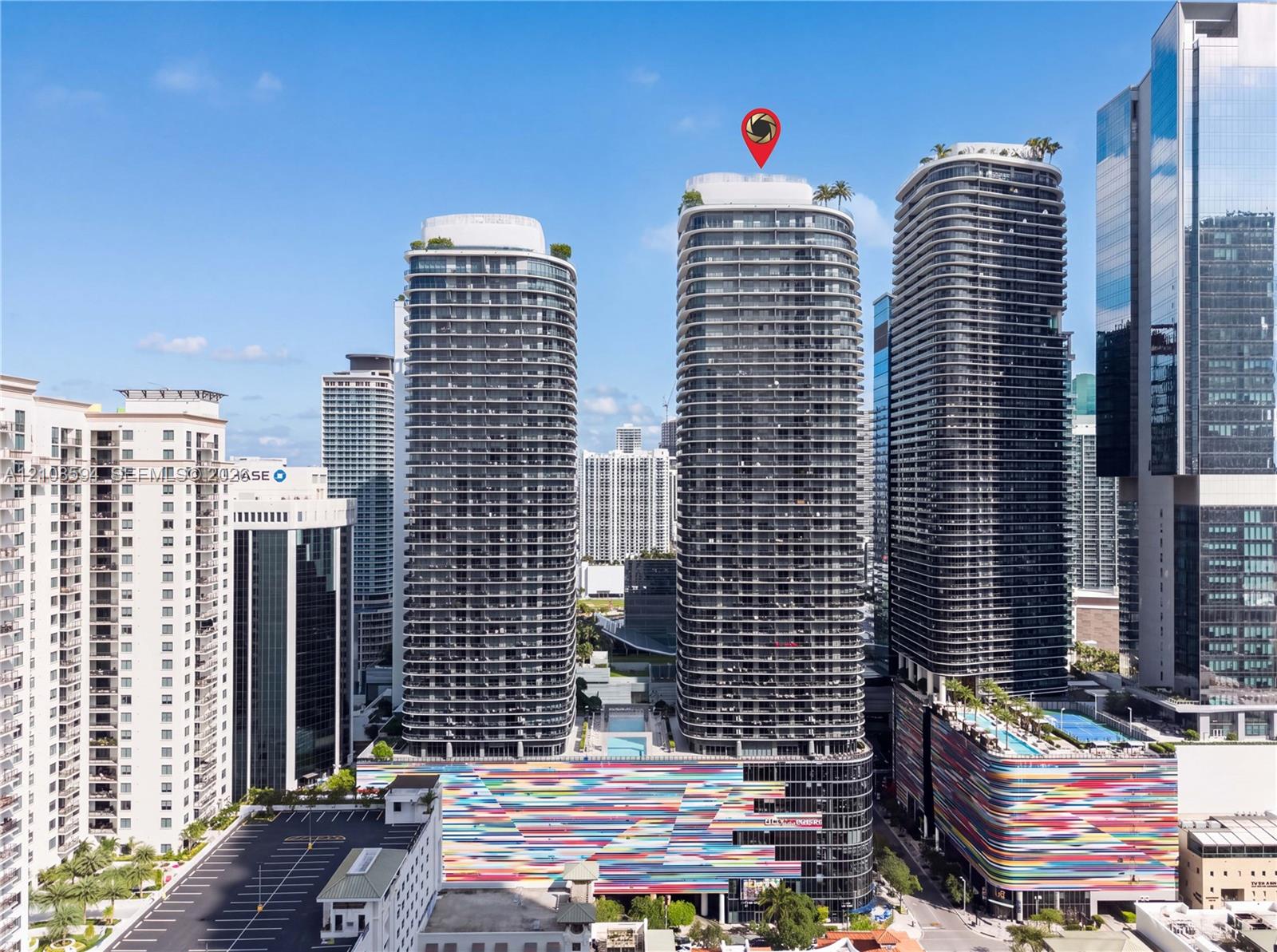 High-rise tower featuring a glass facade, multiple balconies, a rooftop terrace, and architectural detailing with a multi-colored exterior finish