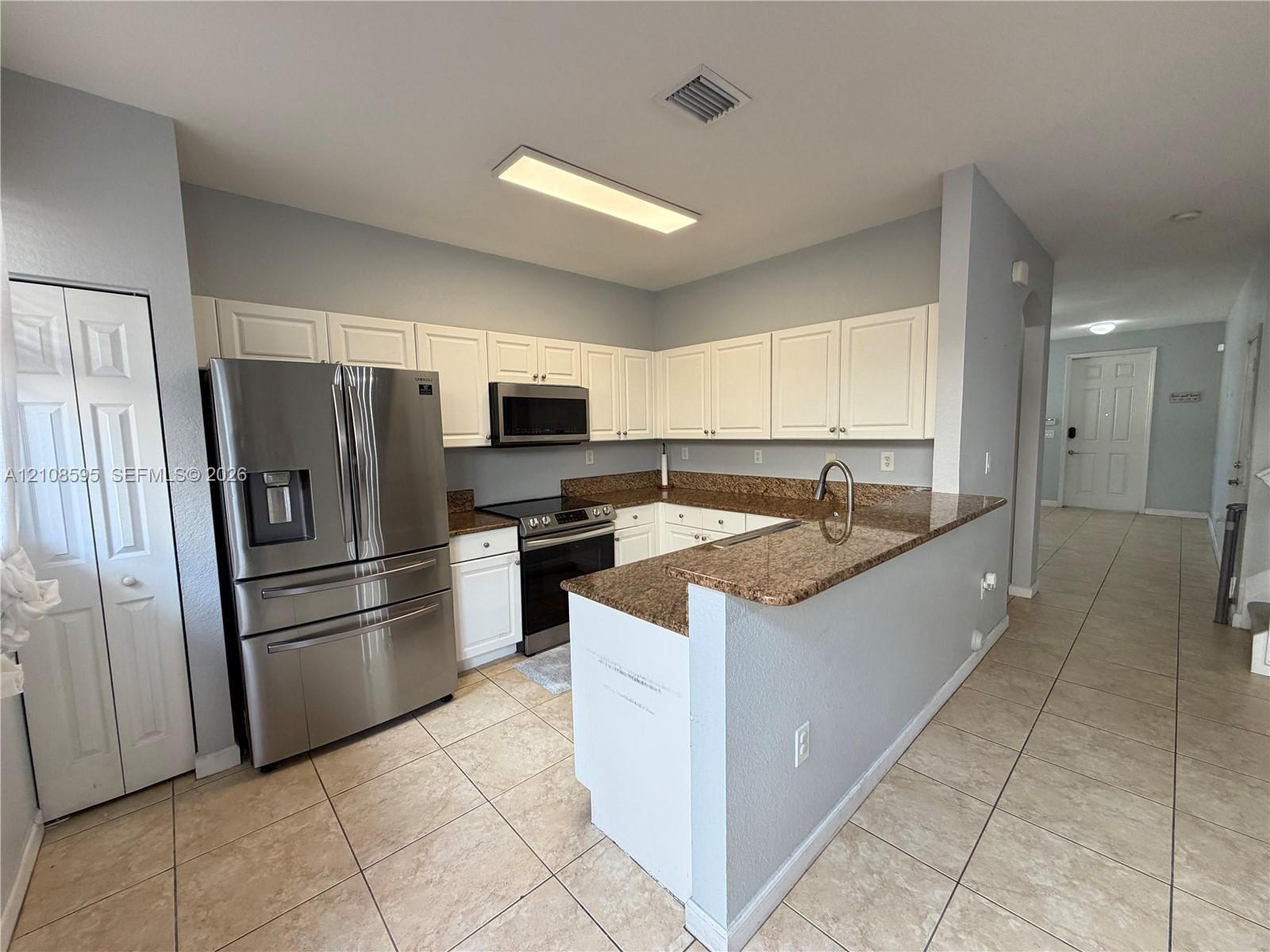 Kitchen featuring white cabinetry, stone-surface countertops, stainless steel appliances, and tile flooring