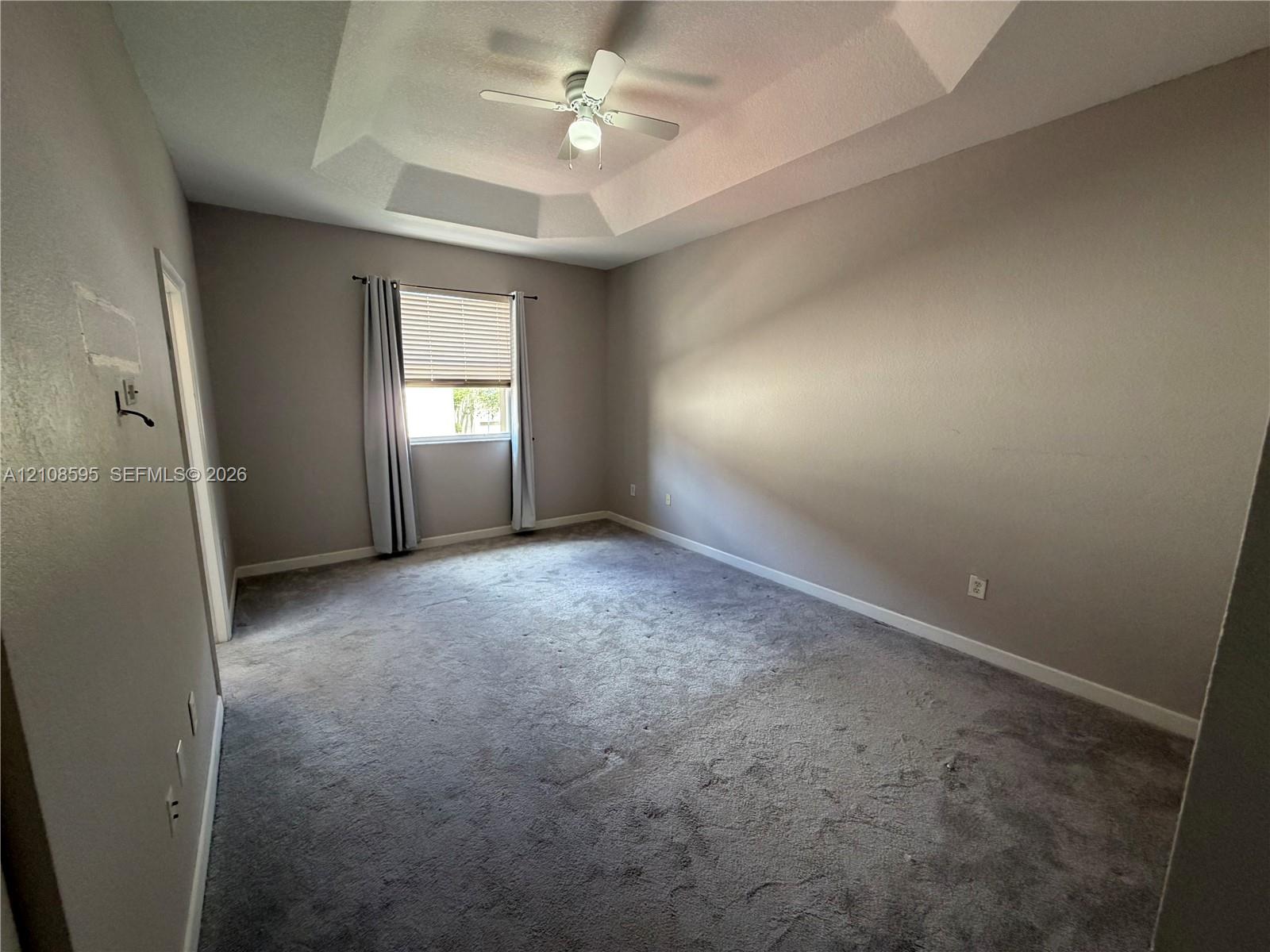 Tray ceiling with a central ceiling fan and neutral wall finish, complemented by wall-to-wall carpeting and an operable window