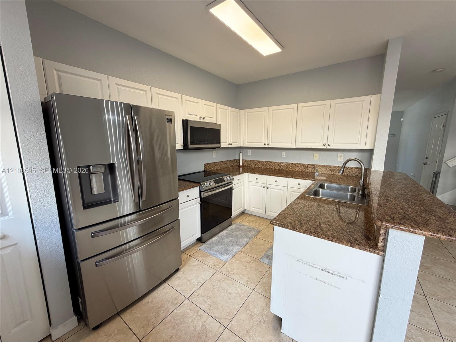 Kitchen featuring white cabinetry, stone-finish countertops, tile flooring, stainless steel French-door refrigerator, and an integrated stainless steel sink with a high-arch faucet