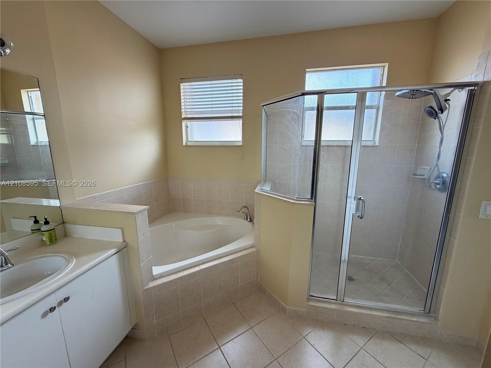 Bathroom featuring a separate garden tub, a corner shower enclosure with glass doors, a vanity with an integrated sink, and tile flooring
