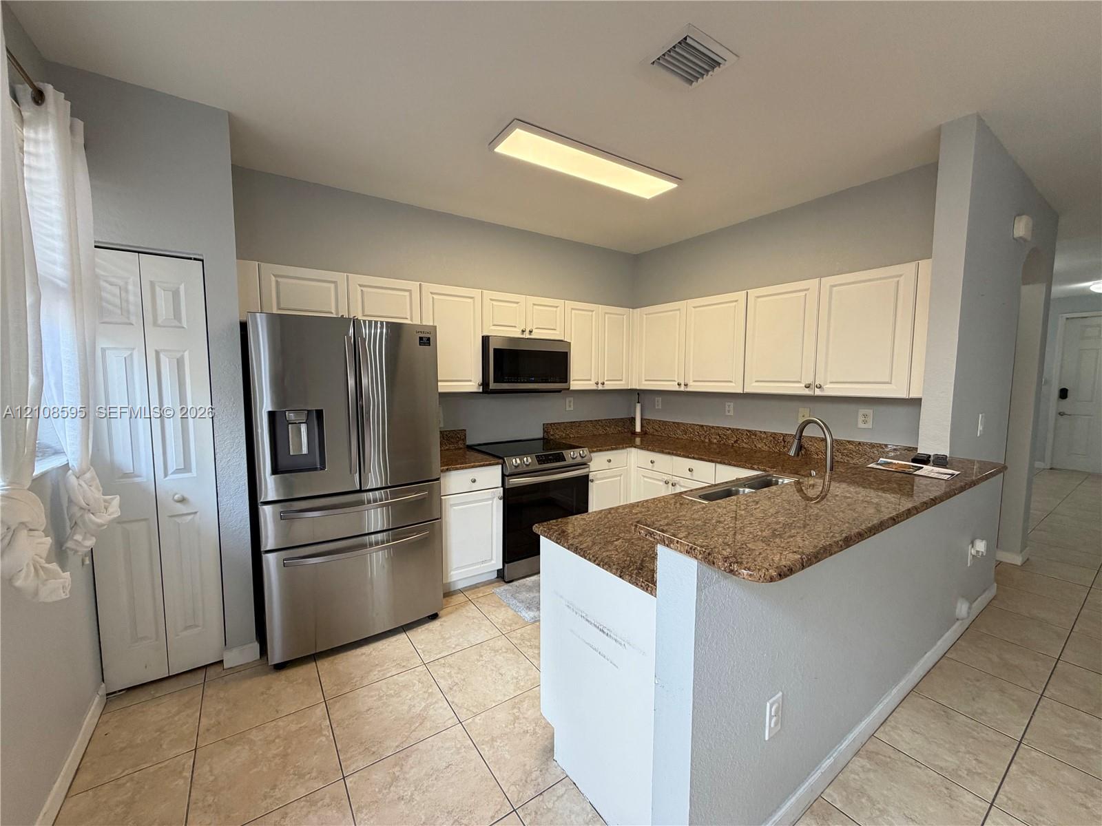 Kitchen featuring white cabinetry, stone countertops, stainless steel appliances, and ceramic tile flooring