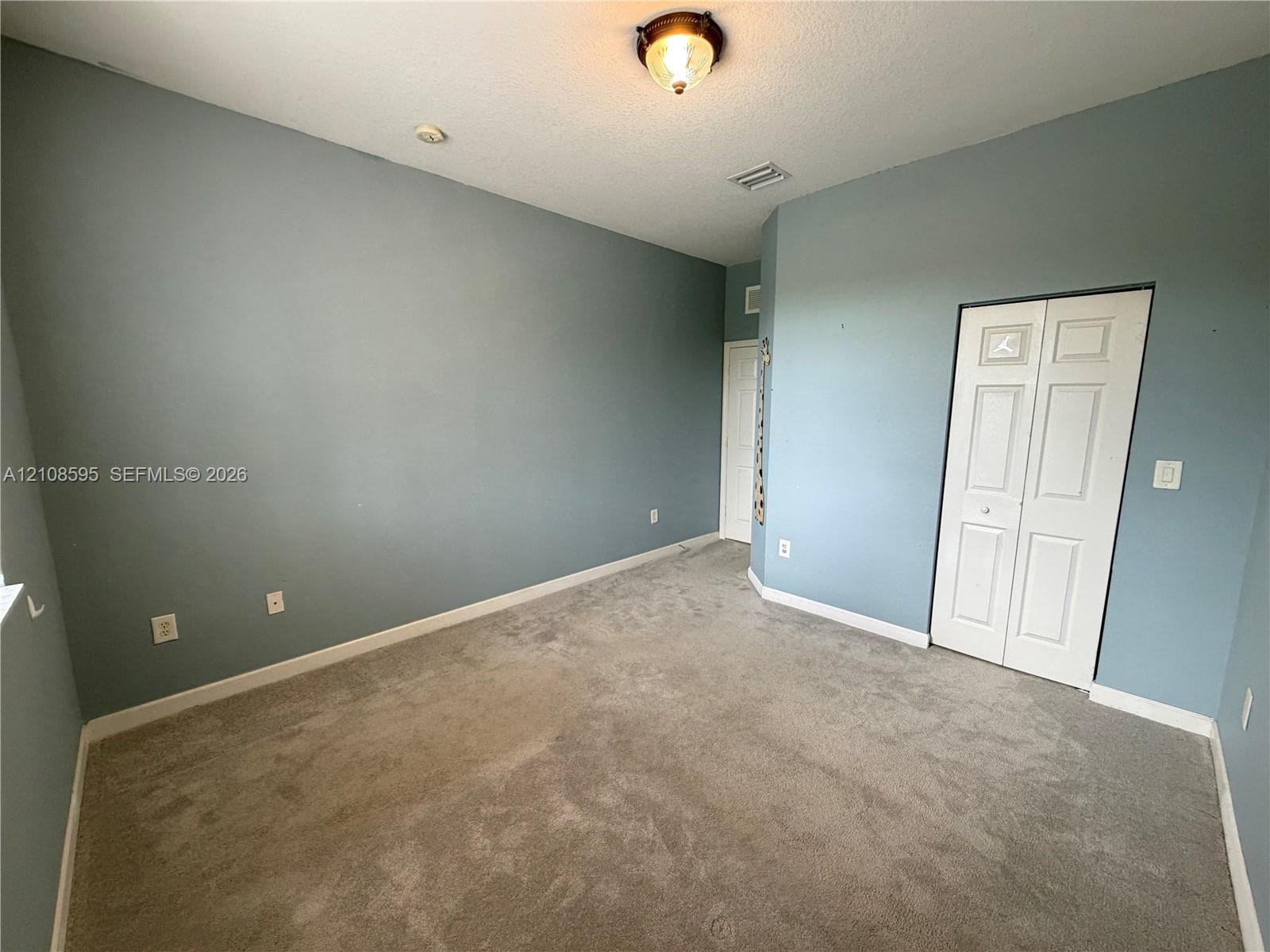 Room featuring neutral wall-to-wall carpeting, flush-mount lighting, and a bi-fold closet door