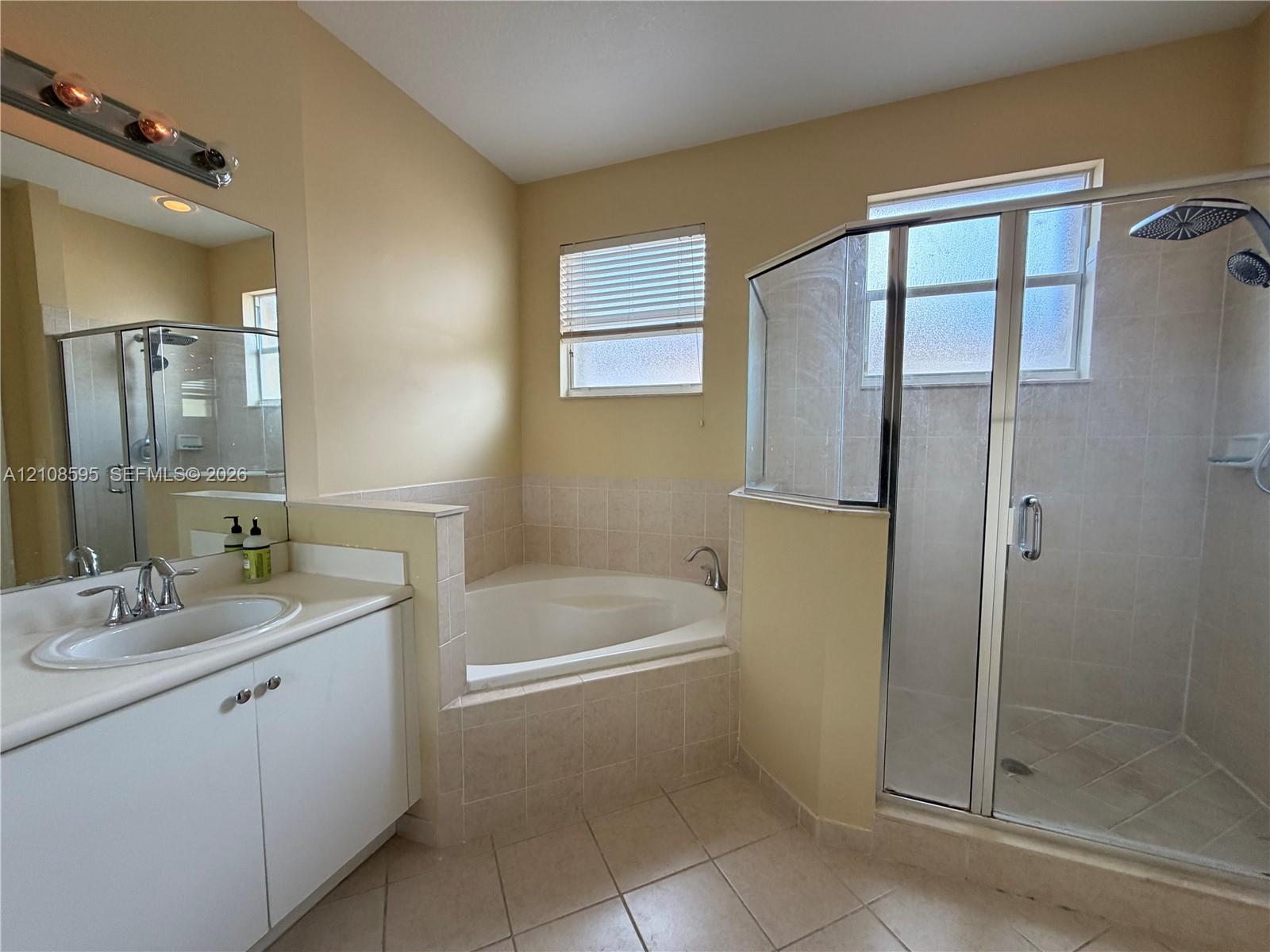 Bathroom featuring a white vanity with a drop-in sink, tile-surround soaking tub, glass-enclosed shower, and tile flooring
