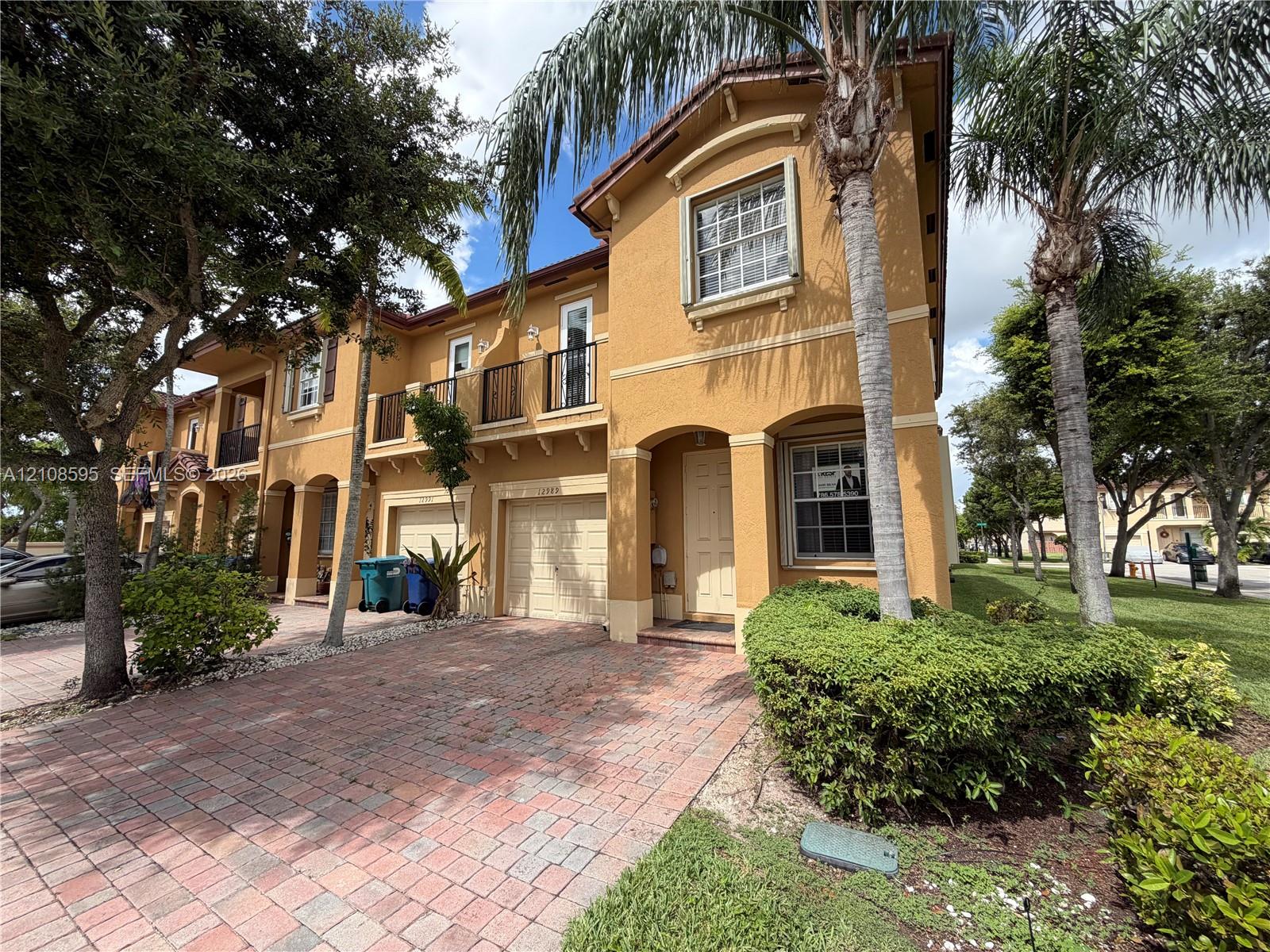 Stucco exterior featuring arched entryways, a paver driveway, an attached garage, and second-story metal-railing balconies