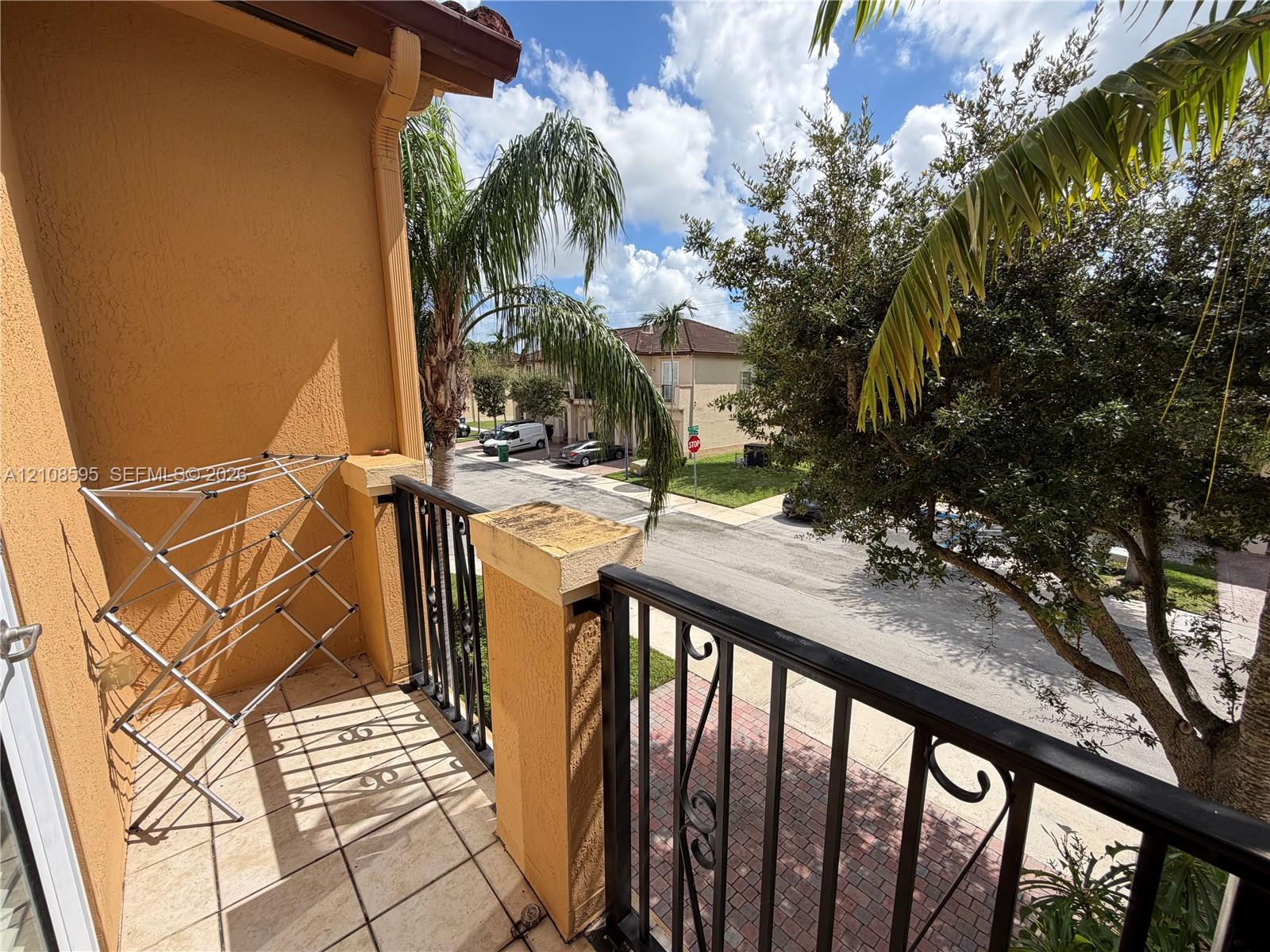 Covered balcony featuring tile flooring, stucco walls, and decorative metal railings with stone-capped pillars