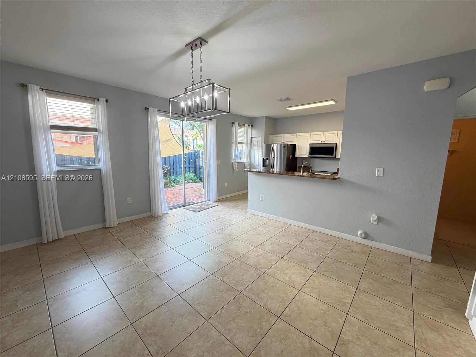Open-concept interior featuring large-format ceramic tile flooring, a geometric metal chandelier, white kitchen cabinetry, and a sliding glass door providing exterior access