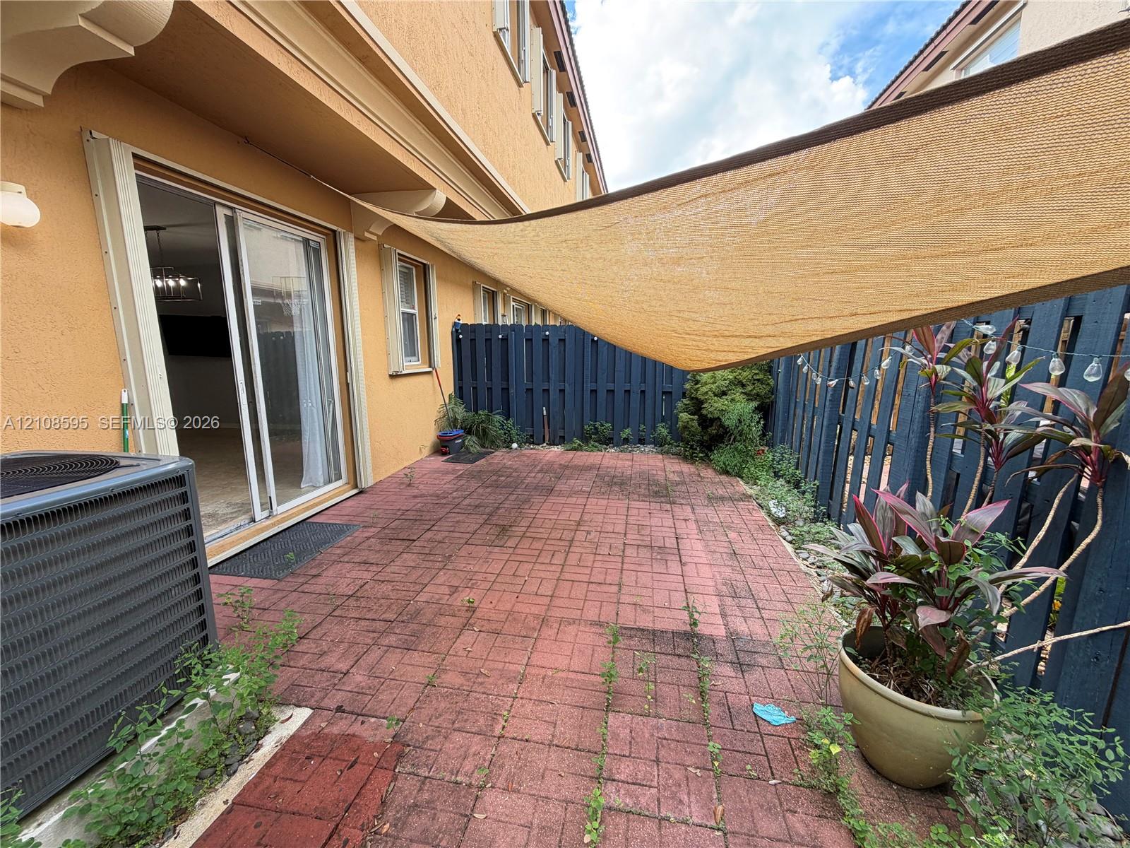 Private patio featuring red brick paving, a retractable overhead shade canopy, and perimeter wood fencing