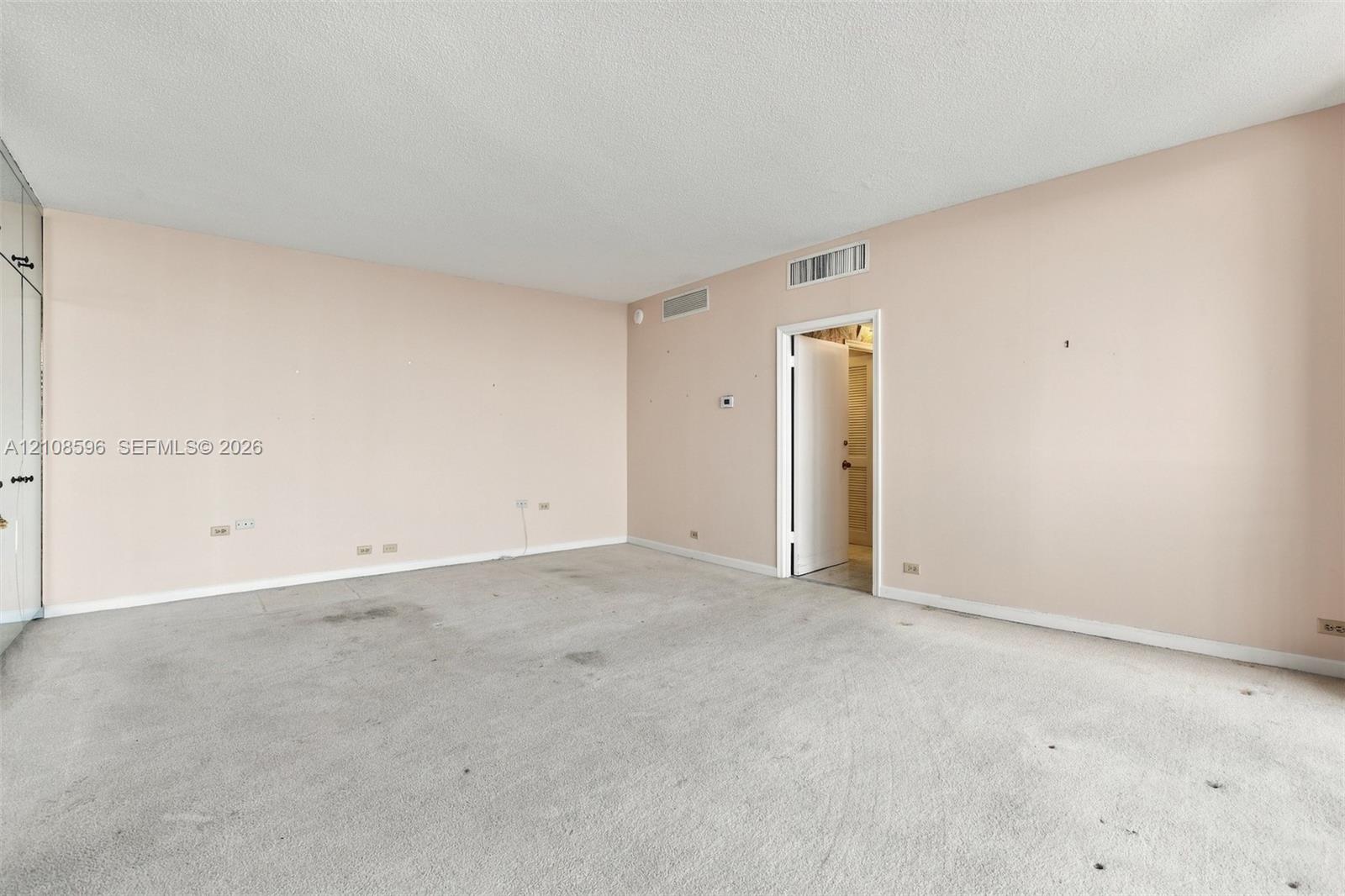 Neutral-toned interior space featuring built-in floor-to-ceiling closets, wall-to-wall carpeting, and a single-panel interior door