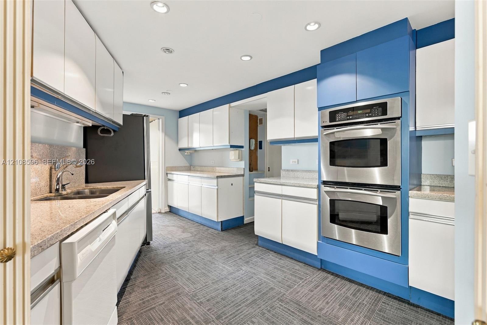 Kitchen featuring white cabinetry with blue accents, stone-composite countertops, built-in stainless steel double wall ovens, recessed lighting, and patterned flooring