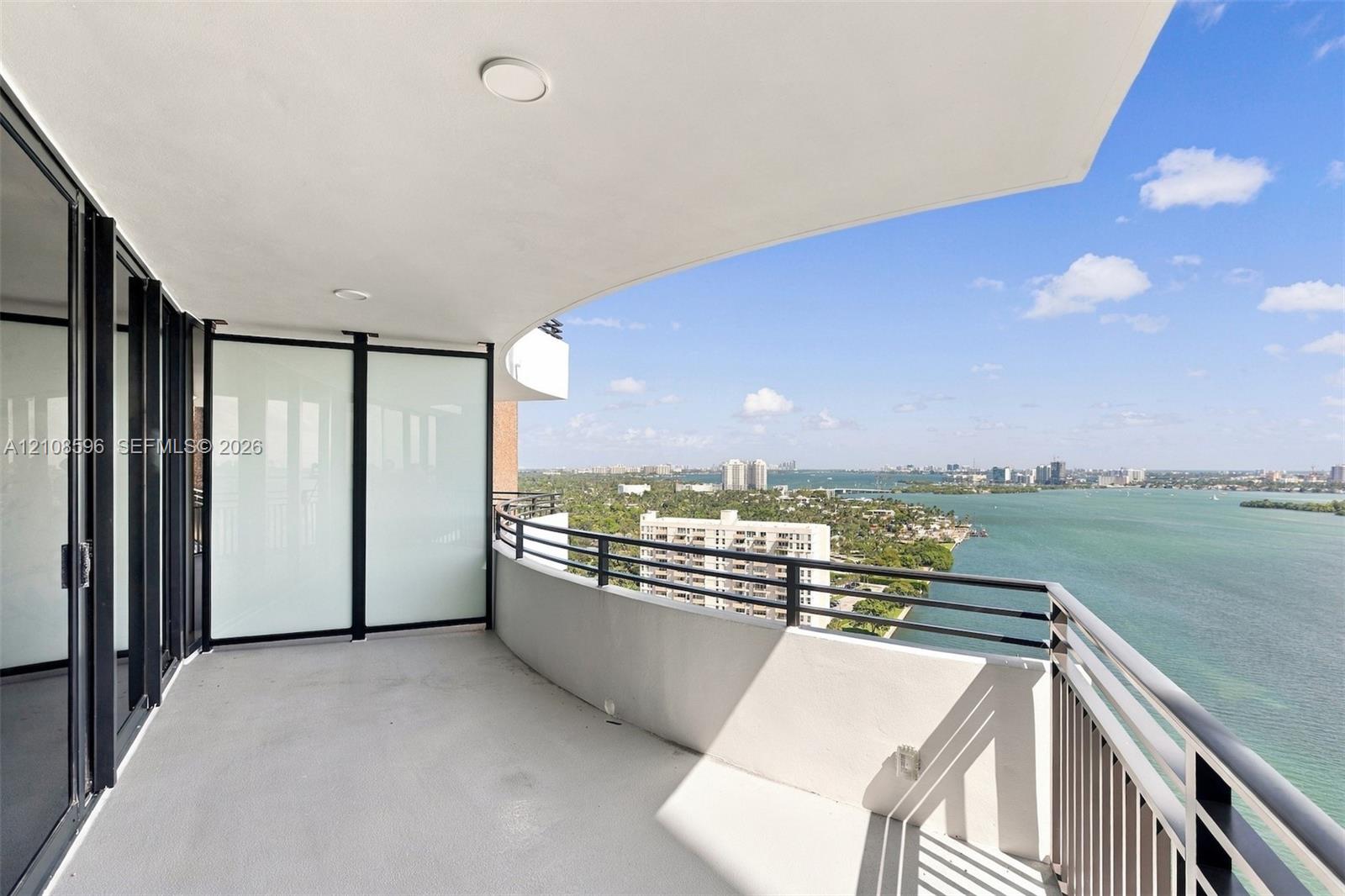 Covered balcony featuring a concrete floor, dark metal railing, recessed ceiling lighting, and frosted glass privacy panels