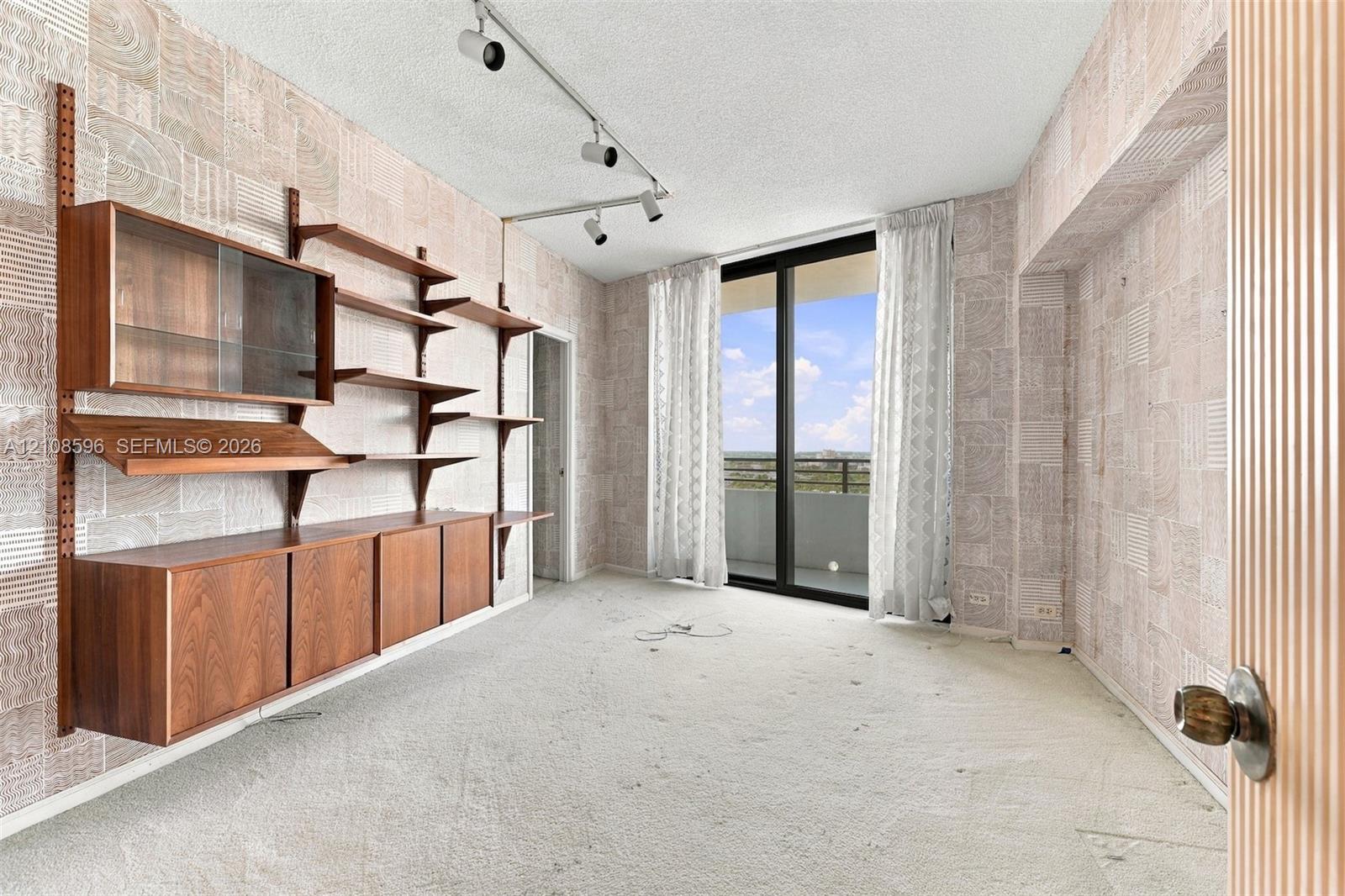Wall-mounted wood cabinetry with shelving, track lighting, sliding glass door, and exterior balcony