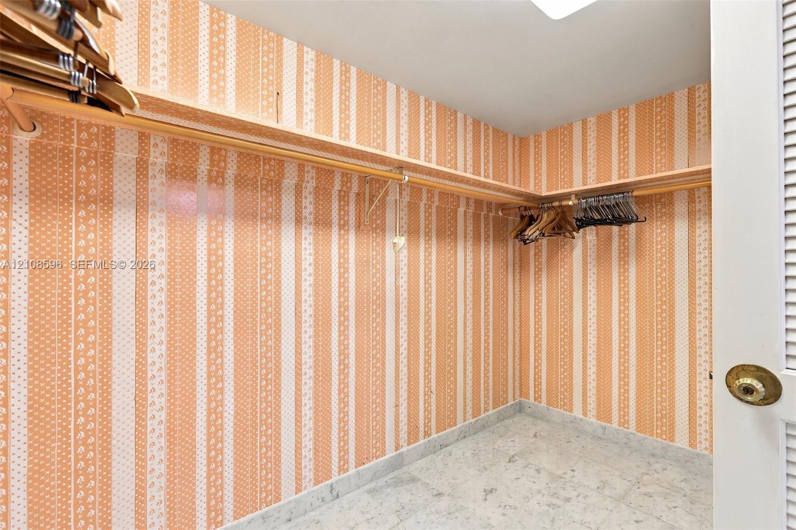 Storage space featuring built-in wooden shelving, patterned wall covering, and stone-finish flooring
