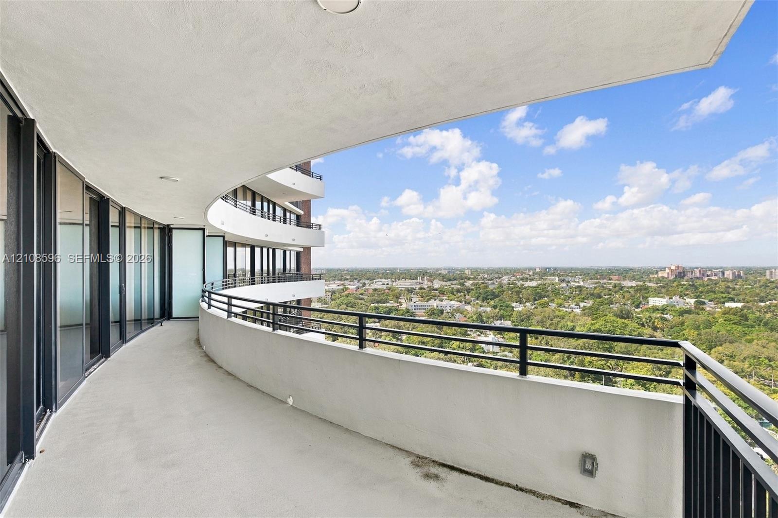 Curved exterior balcony featuring concrete flooring, a solid half-wall, and black metal railings with panoramic outdoor surroundings