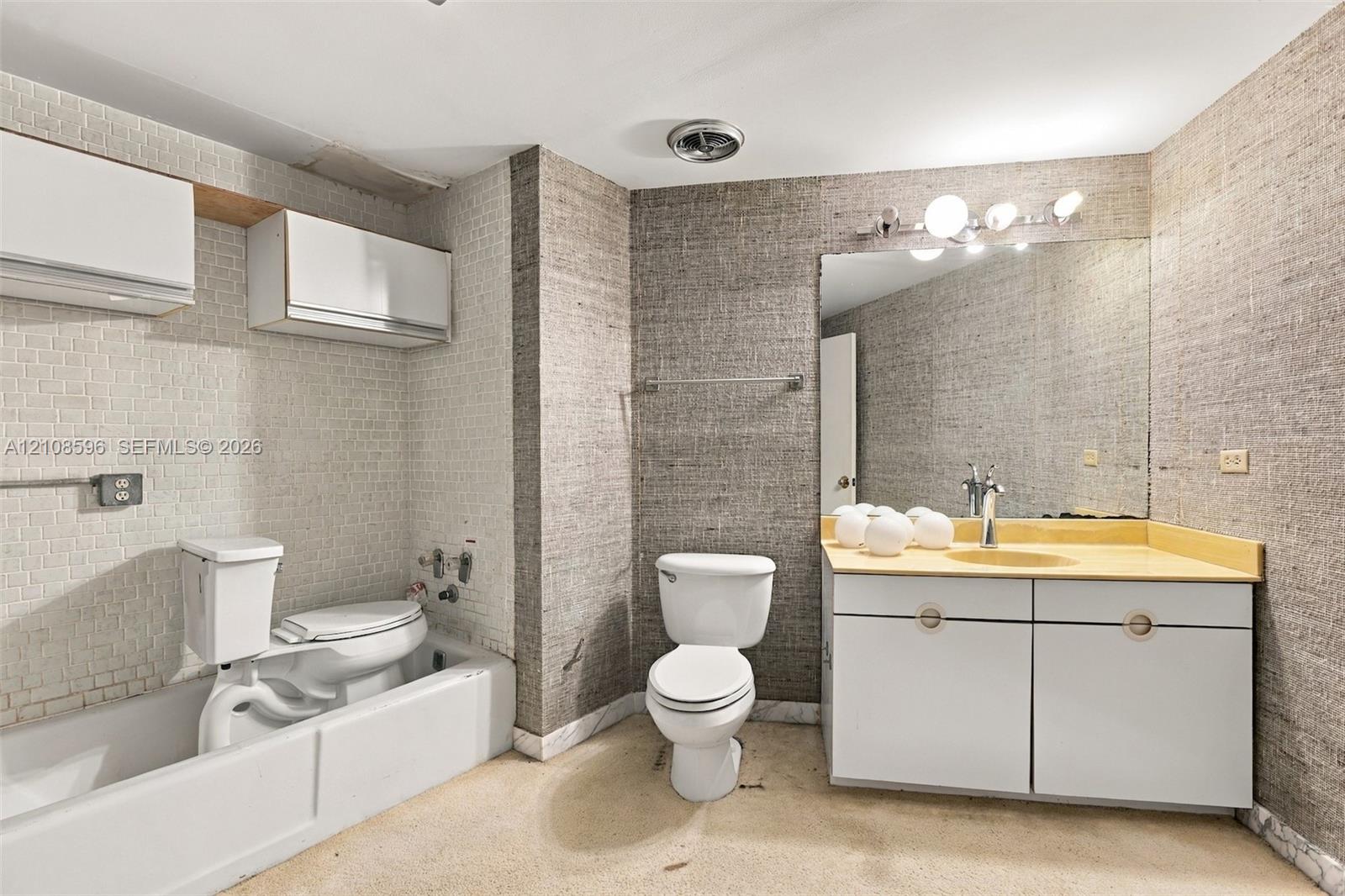 Bathroom featuring textured wall coverings, wall-mounted white cabinetry, a single vanity with integrated sink, and a combination tub and shower