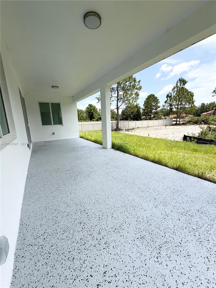 Covered concrete patio featuring a speckled epoxy finish, flush-mount ceiling lighting, and support columns