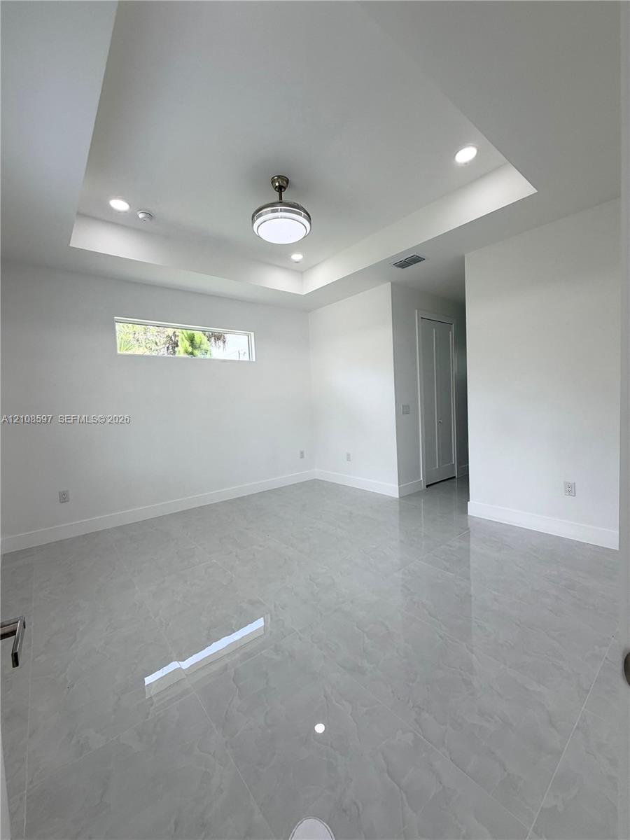 Tray ceiling with recessed lighting, large-format tile flooring, central ceiling fan, and horizontal clerestory window