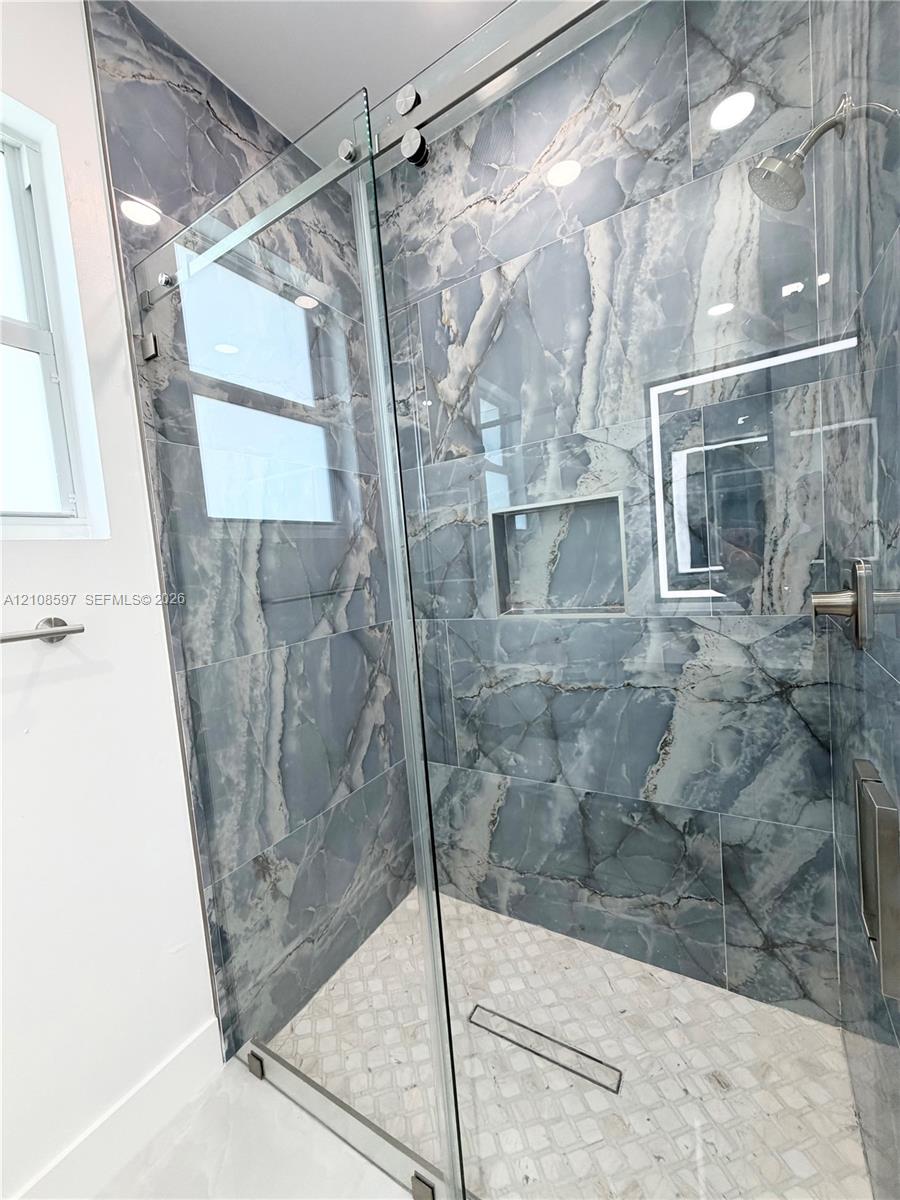 Walk-in shower with floor-to-ceiling large-format tile, frameless glass sliding enclosure, built-in wall niche, brushed metal shower head, and mosaic tile flooring