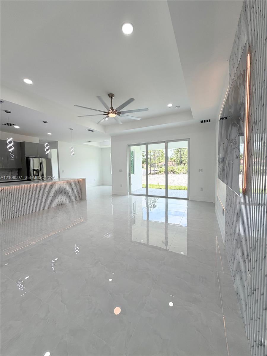 Open-concept area featuring polished stone-finish flooring, recessed lighting, a coffered ceiling with a modern multi-blade ceiling fan, and a kitchen island with stone-finish cladding