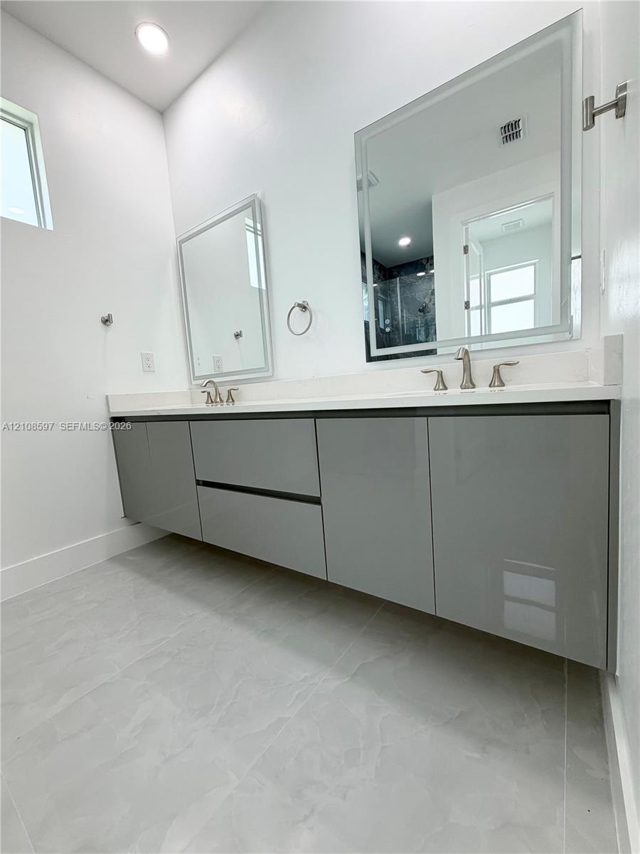 Floating dual vanity with high-gloss gray cabinetry, white stone-finish countertop, undermount sinks, and LED-backlit vanity mirrors