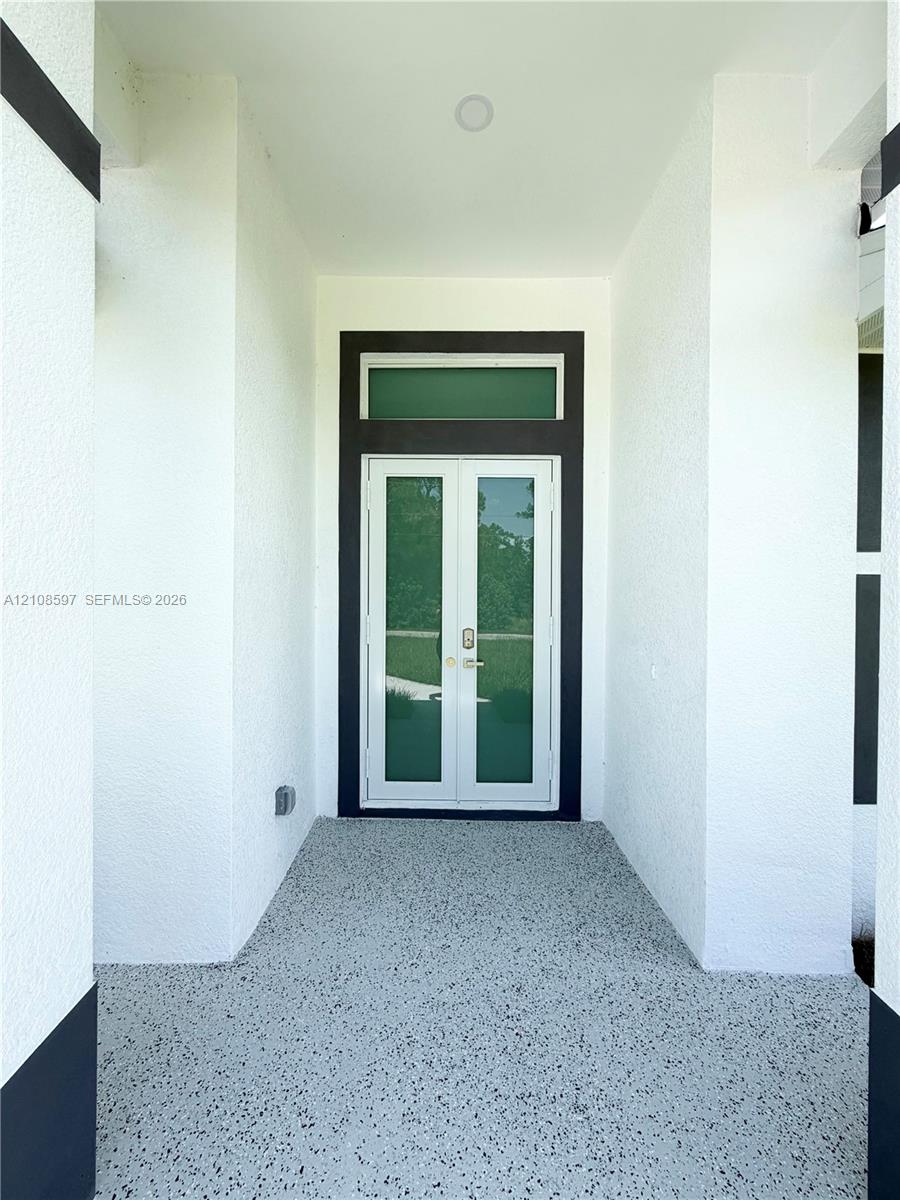 Covered entryway featuring a stippled-texture ceiling, recessed lighting, aggregate flooring, and a double-door entry with a rectangular transom window
