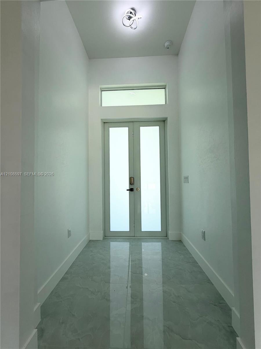 Entryway featuring double glass-paneled doors, transom window, high ceilings, large-format polished stone-finish tile flooring, and contemporary flush-mount overhead lighting