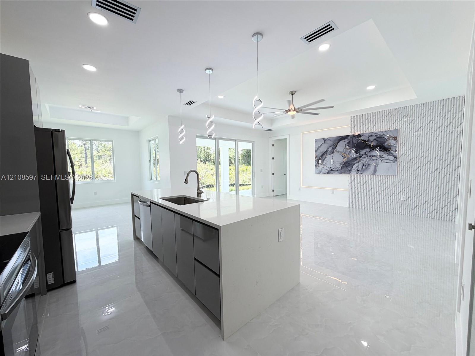 Open-concept kitchen featuring an oversized island with quartz countertops, custom cabinetry, recessed lighting, stone-finish wall cladding, and oversized light-colored floor tiles