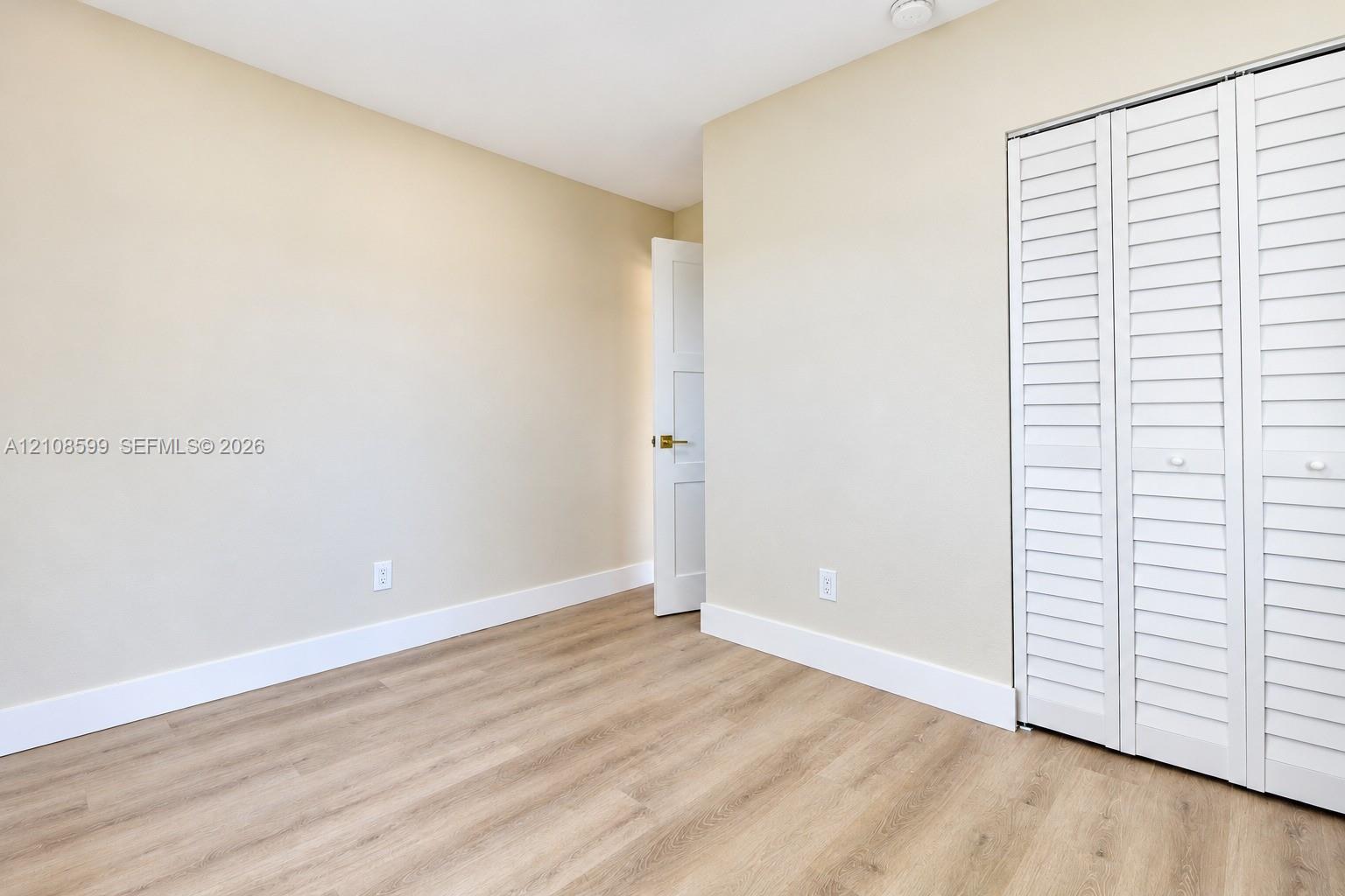 Interior room featuring wood-finish flooring, white louvered closet doors, and neutral wall paint