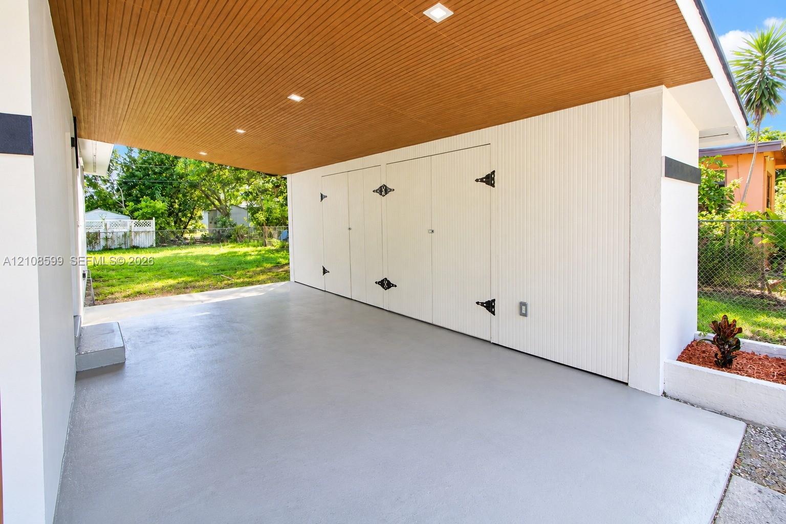 Covered carport featuring a wood-slat ceiling, recessed lighting, concrete flooring, and integrated storage cabinetry with decorative hardware