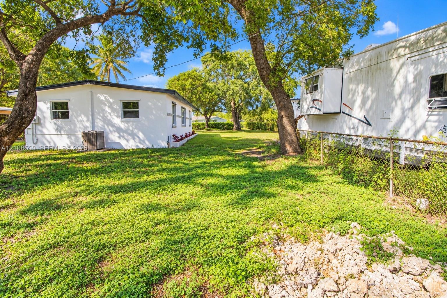 Expansive grounds featuring mature shade trees, a grass lawn, and chain-link fencing