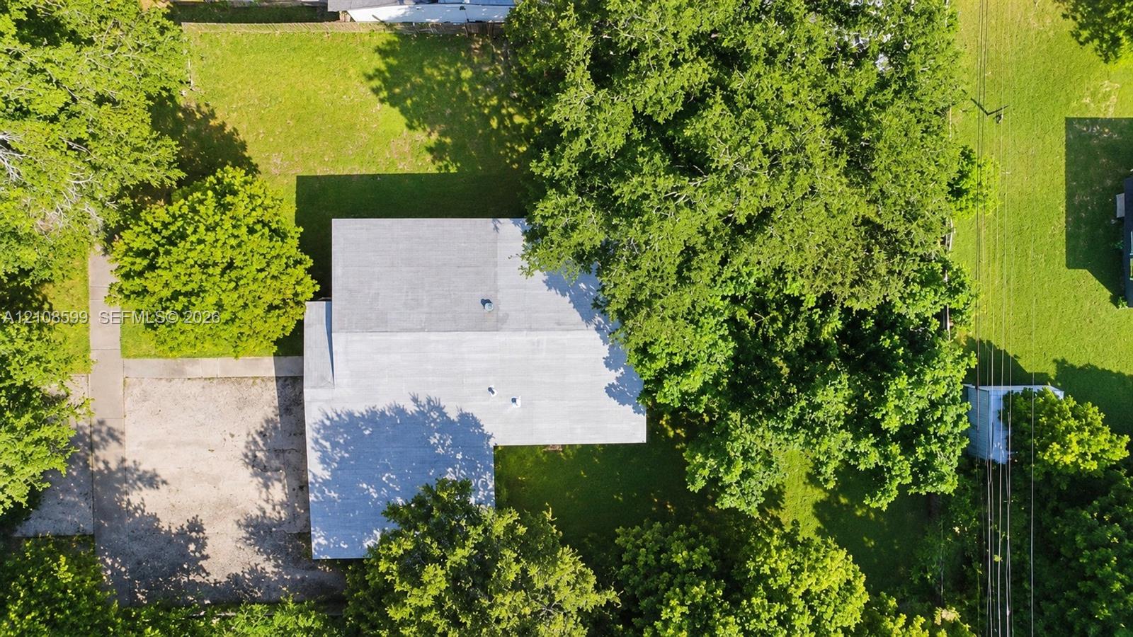 Aerial perspective featuring a spacious lot with mature trees and a concrete driveway
