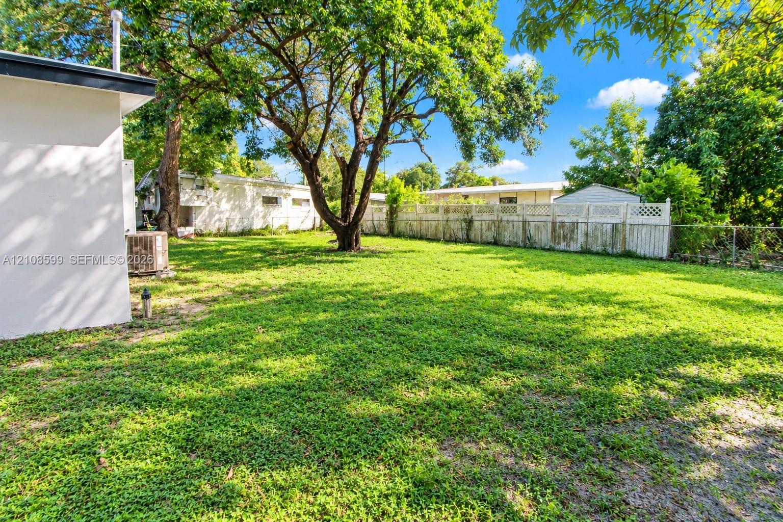 Expansive backyard featuring a lush lawn, mature trees, and a white privacy fence