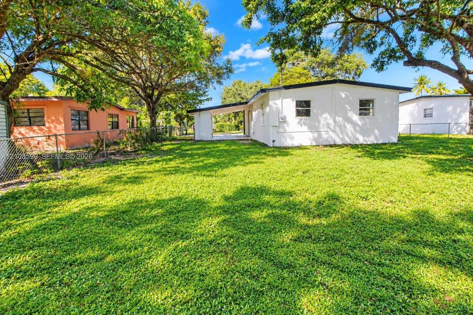 Expansive green lawn featuring mature shade trees and a covered rear patio