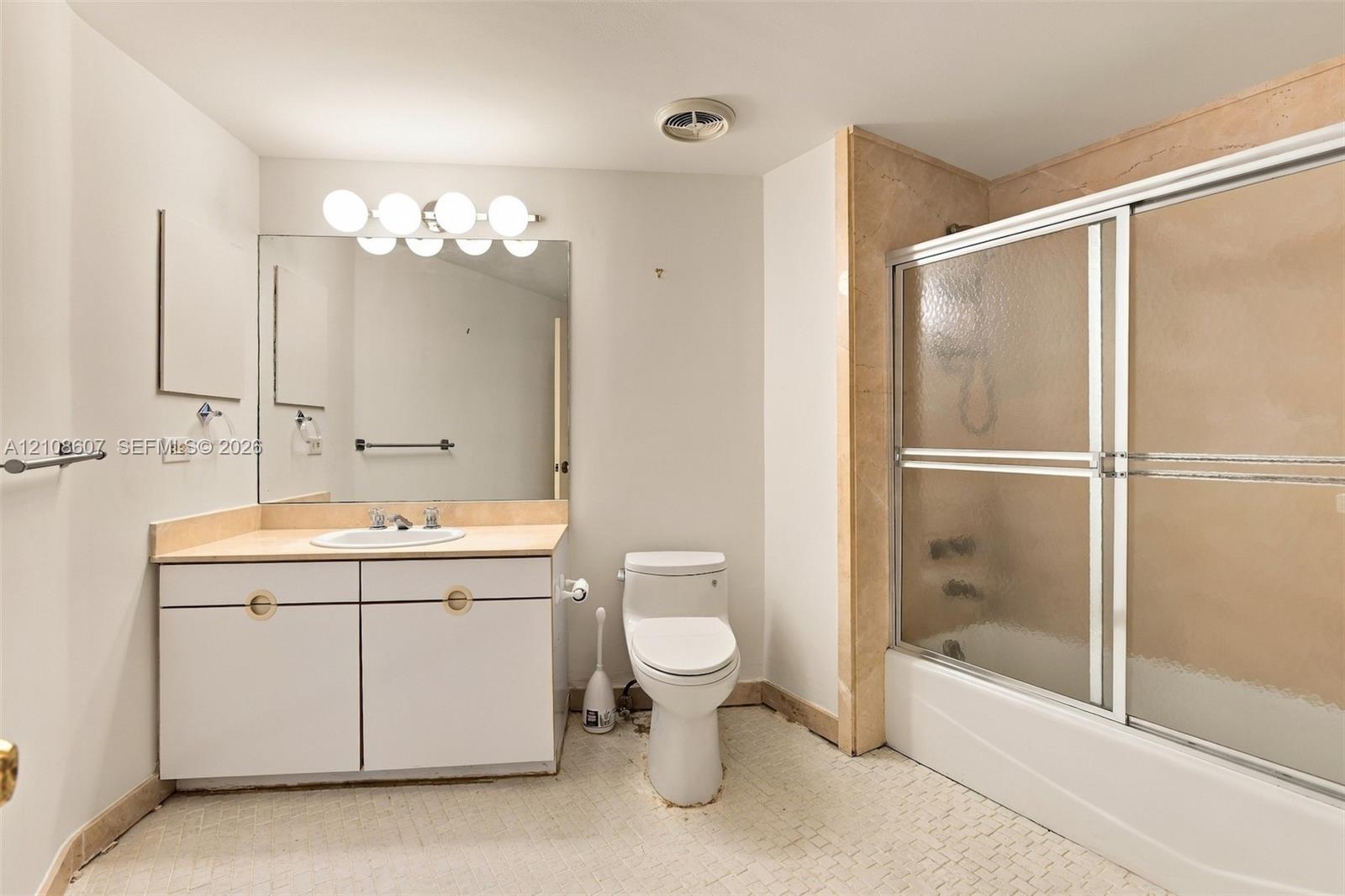 Bathroom featuring a vanity with integrated sink and stone-surfaced countertop, wall-to-wall mirror, five-light fixture, and a tub-shower combination with sliding glass doors and stone surround