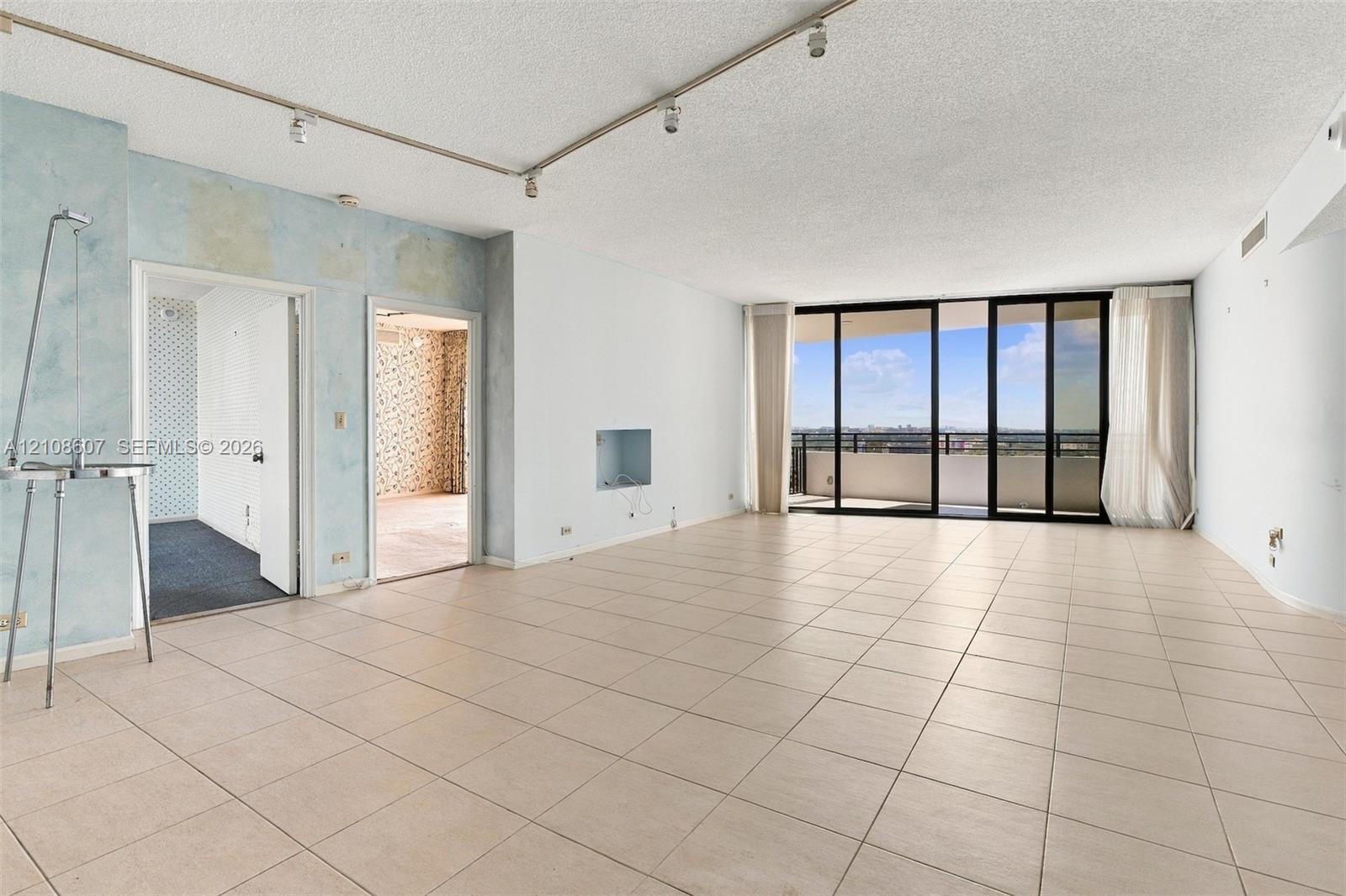 Open-concept floor plan featuring ceramic tile flooring, built-in track lighting, and floor-to-ceiling glass sliding doors opening to a balcony