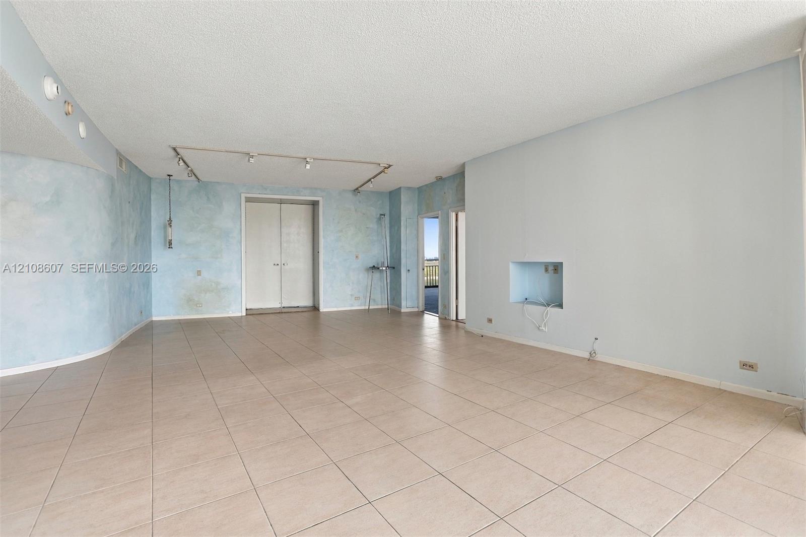 Open-concept interior featuring large-format ceramic tile flooring, textured wall treatments, adjustable track lighting, and a recessed wall niche