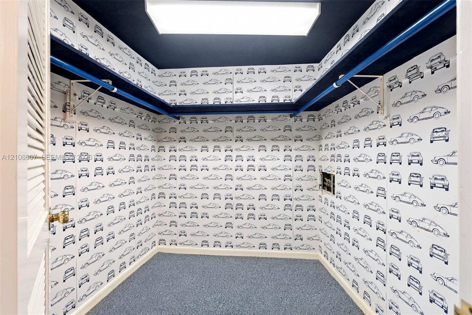 Walk-in storage space featuring wrap-around shelving, a ceiling-mounted light fixture, and louvered door access